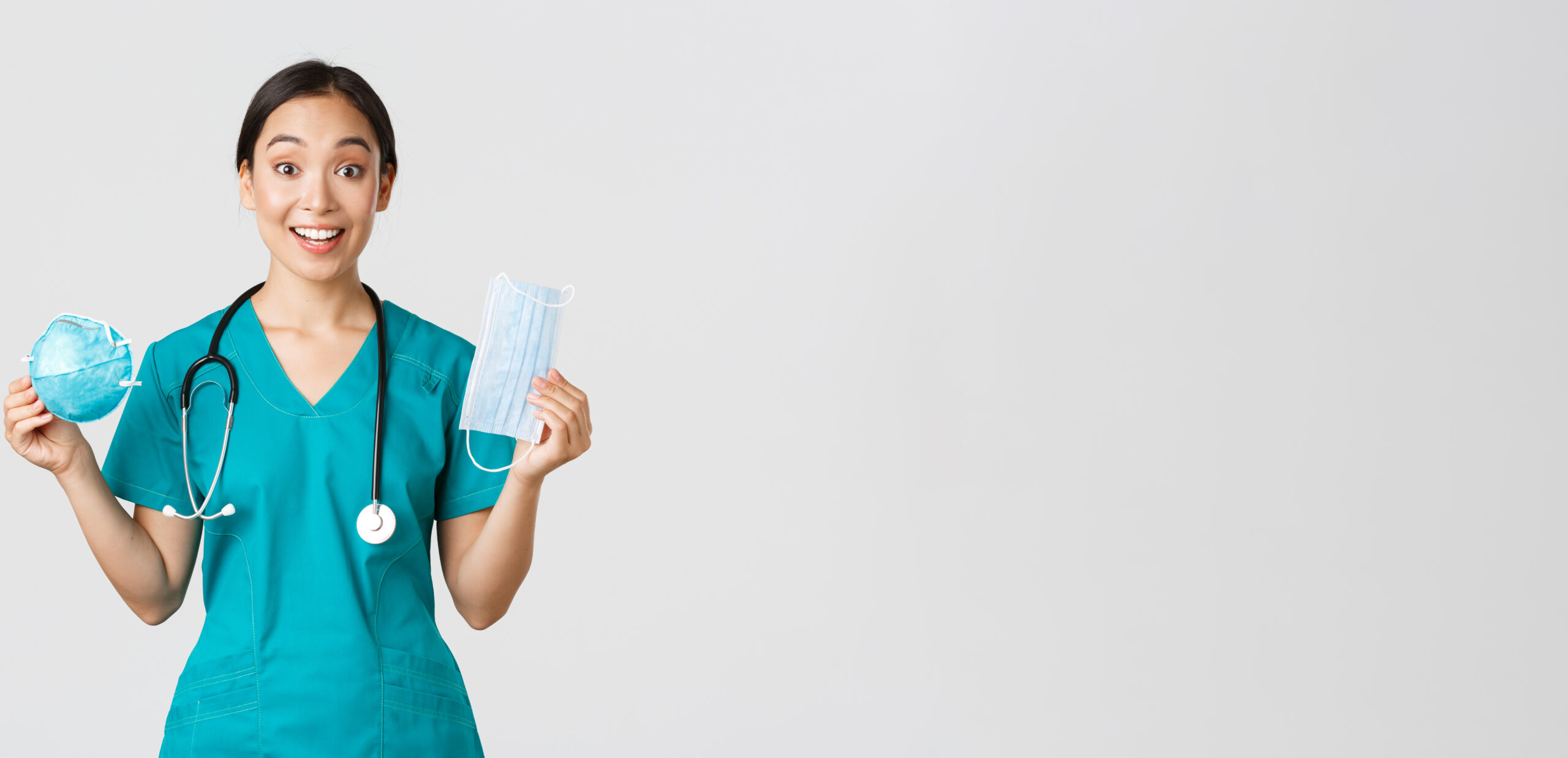 covid 19, coronavirus disease, healthcare workers concept. amused smiling asian female nurse, inters in scrubs showing respirator and medical mask, receive personal protective equipment